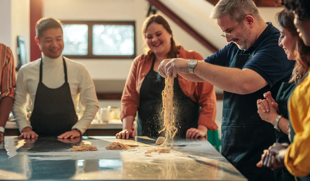 people standing at a cooking class with a man making pasta